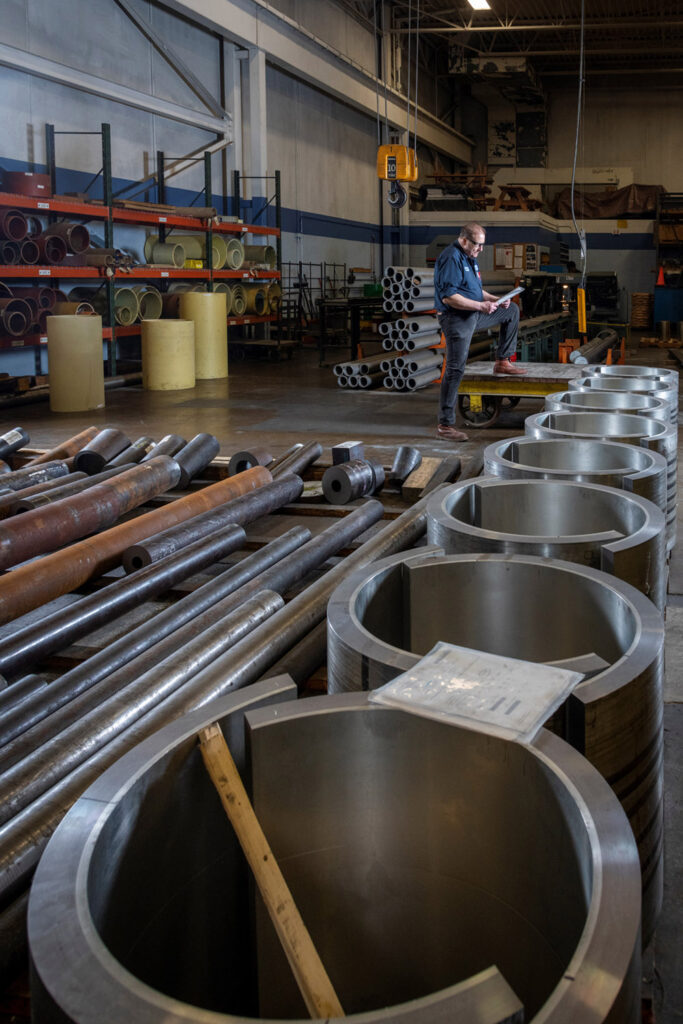 Team member Frank reading shop packet amidst raw material, a crane behind him and controller in the foreground.