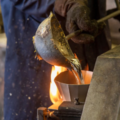 Team member George's hand shown pouring hot babbitt from a heavy ladle into a receptacle.